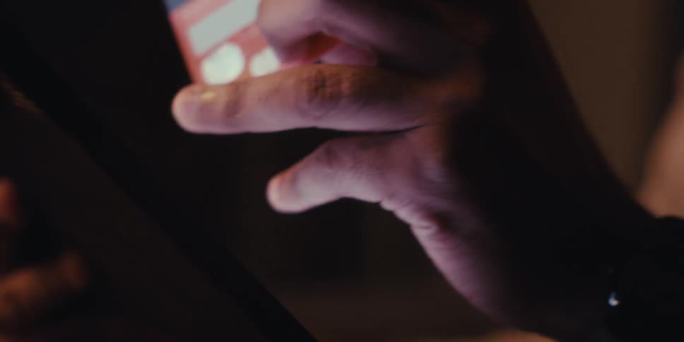 A mans hand holds a credit card while shopping on a tablet in a dimly lit room