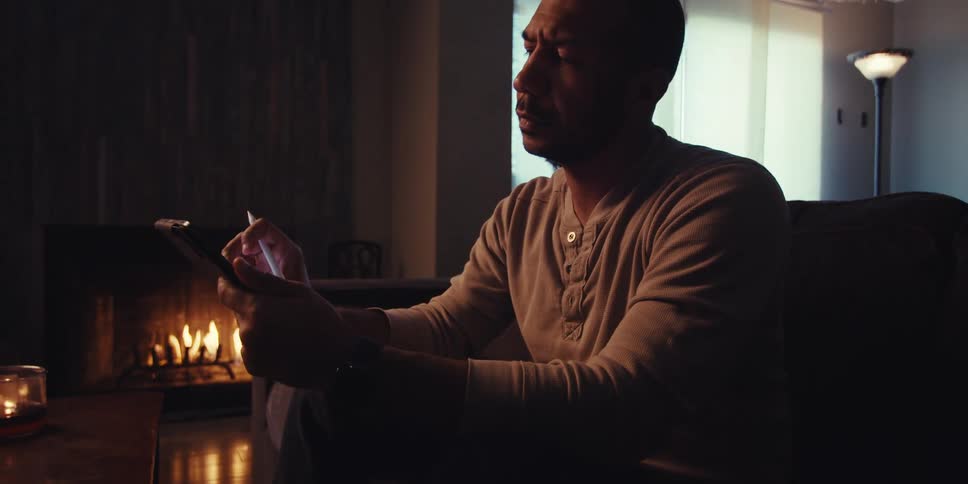 A man with his hand on his chin looks thoughtful and then starts tapping on his tablet screen