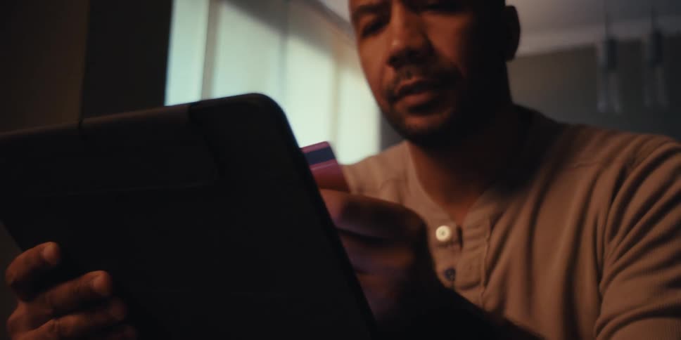 Man enters his credit card information onto his tablet while sitting indoors