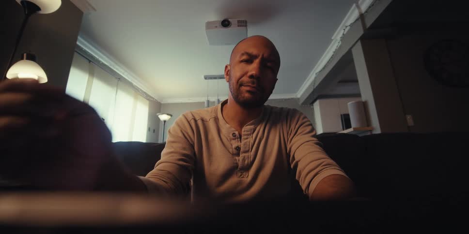 Man sitting on sofa in living room and interacting with electronic device