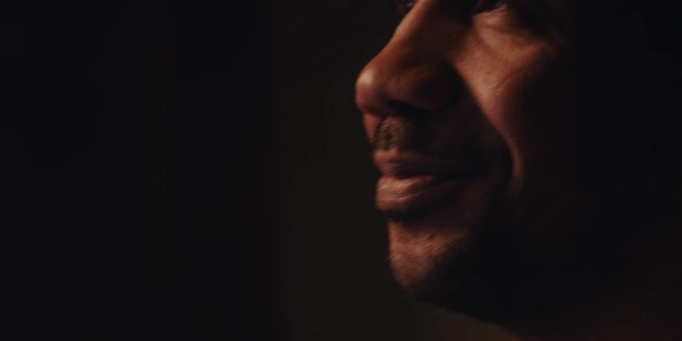 A closeup shows a mans face in a dimly lit room near a fireplace holding a tablet and a credit card