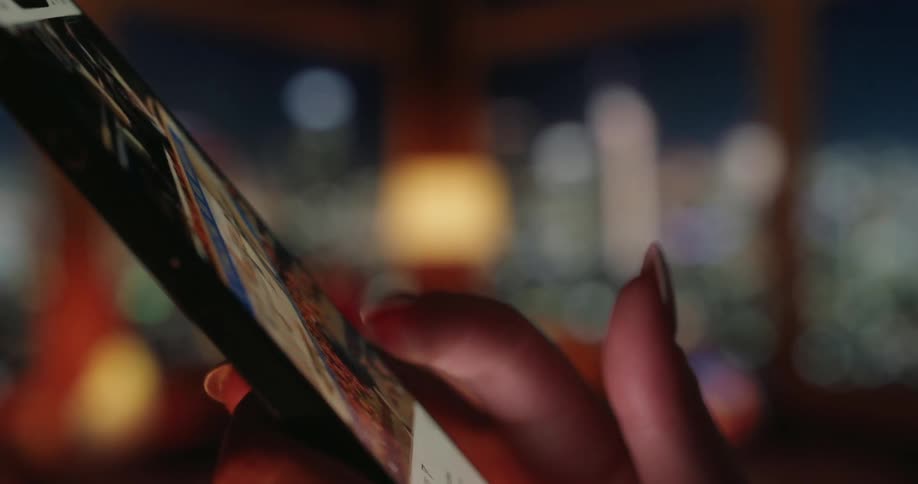 In a blurred indoor setting at night a womans hand interacts with a smartphone screen