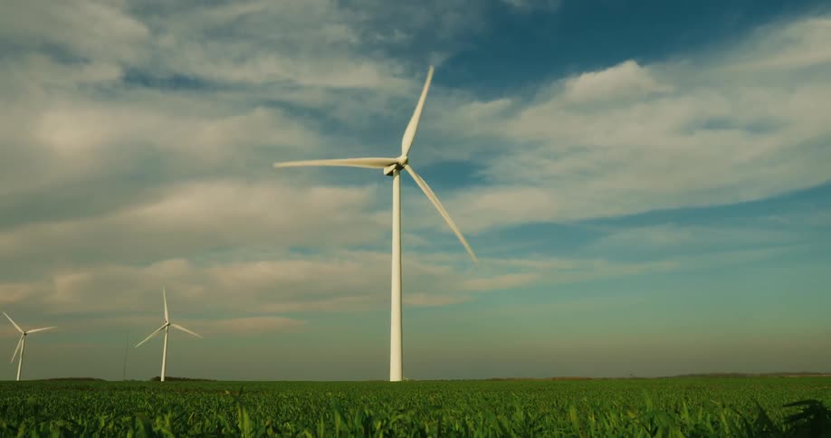 A wind turbine stands tall in a green field under a partly cloudy sky with another turbine visible in the distance