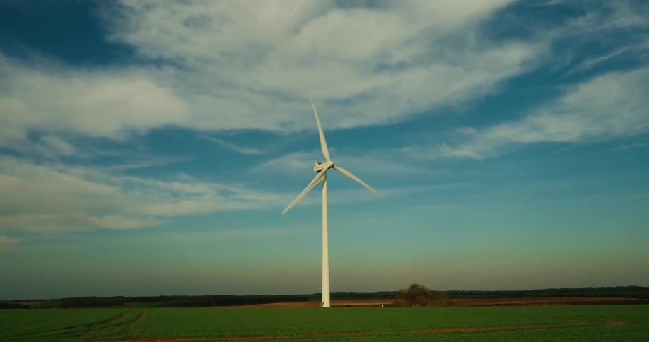 A wind turbine spins over a green field beneath a blue sky streaked with white clouds