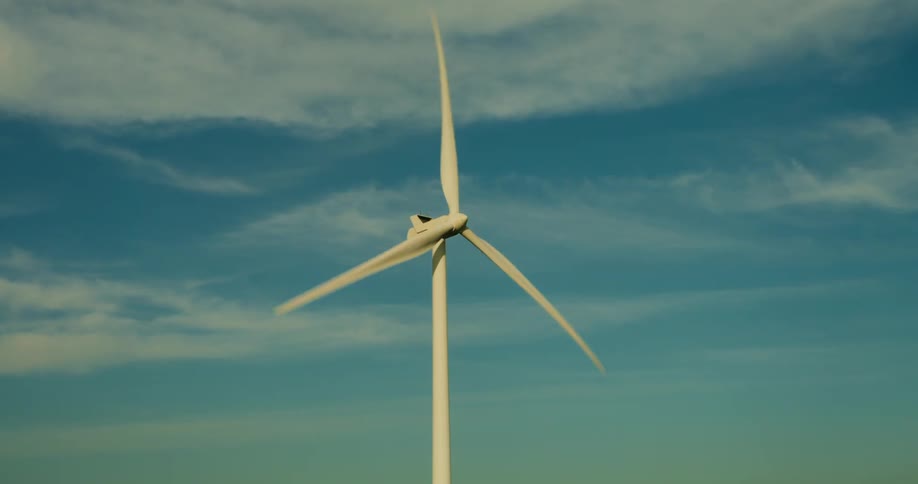 A lone wind turbine stands prominently against a backdrop of a blue sky with scattered clouds with a watermark partially obscuring the view