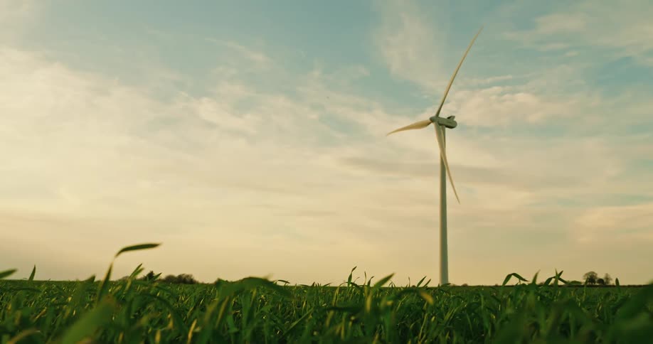 A wind turbine stands tall in a field of green grass under a partly cloudy sky