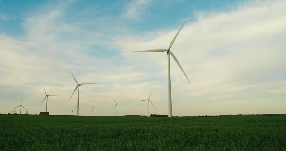 Multiple wind turbines stand tall in a green field against a cloudy sky