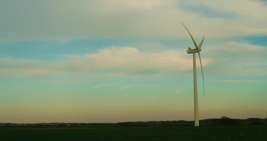 A lone wind turbine stands tall against a backdrop of a vast sky with scattered clouds and a distant horizon