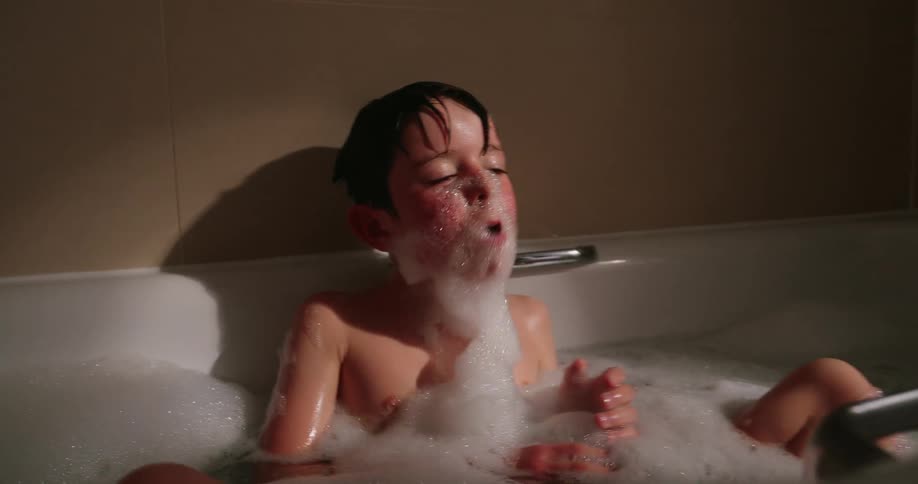 Boy in a bathtub putting foam on his face