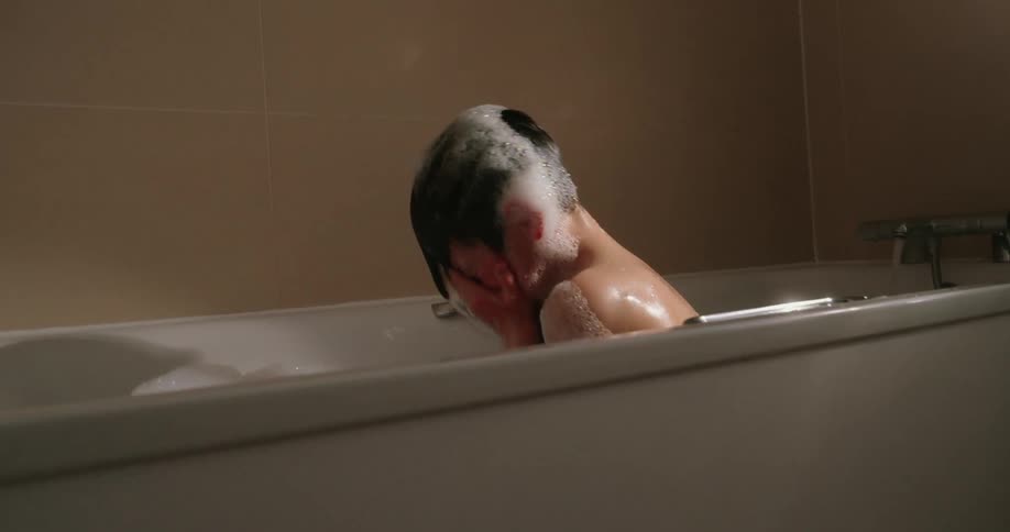 Boy taking a bubble bath lifts his head from the water