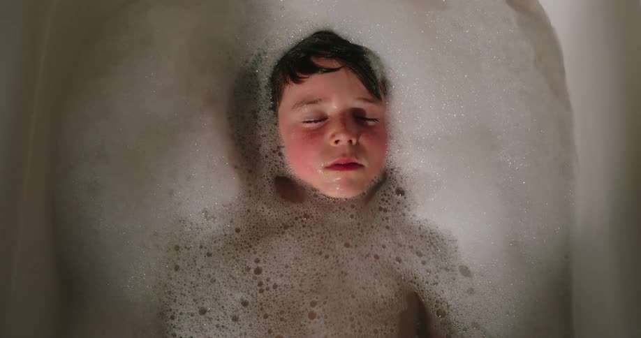 Boy lying in a bathtub with water and foam