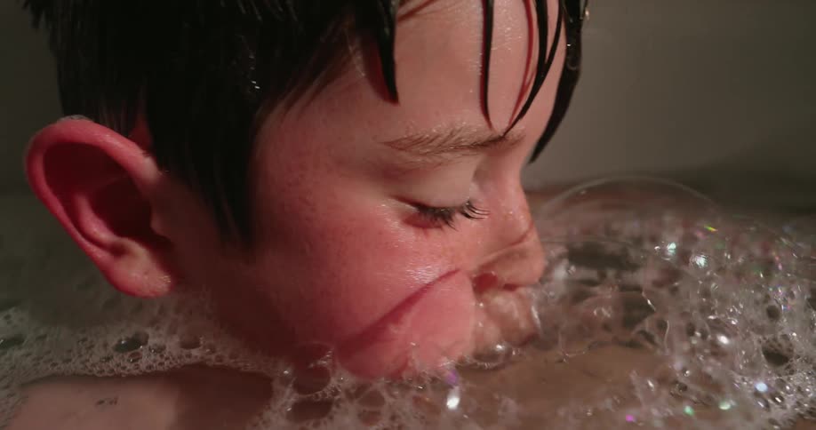 The little boy is blowing bubbles in the bath tub