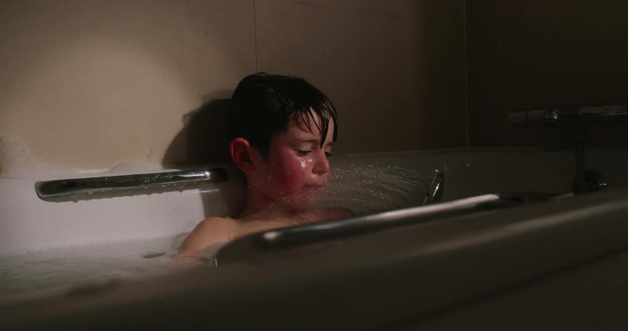 Young boy plays with the shower head while in a bath