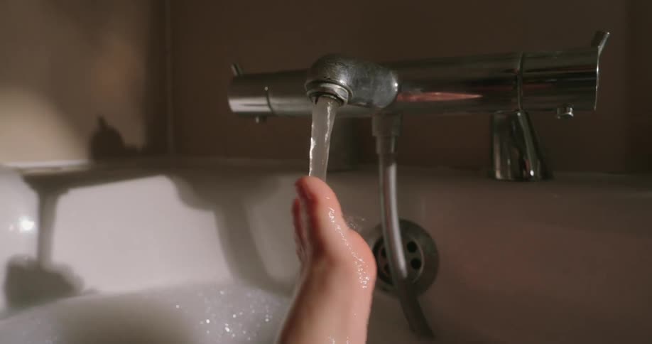 Foot is shown close up with water flowing from a tap over it in a bathtub