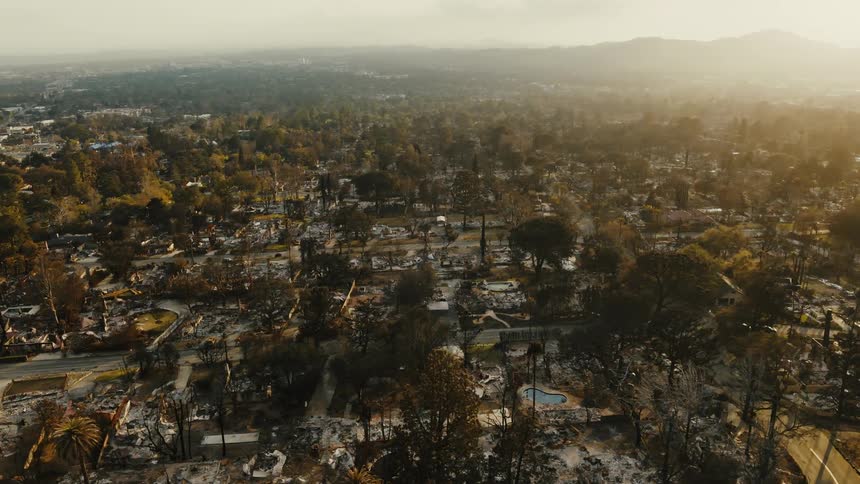 An aerial view reveals the devastating aftermath of a wildfire in a suburban area showing charred remains of homes and trees
