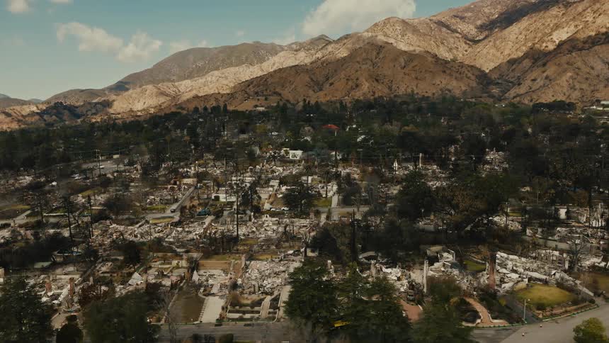 An aerial drone captures the utter ruin of a once lively neighborhood revealing homes rendered to ashes trees charred and a somber stillness across the devastated landscape against the backdrop of the mountains