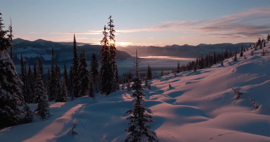 Aerial view of a snow covered mountain ridge and the woods in a valley at sunset