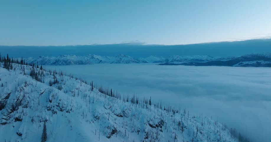 A fog covered lake surrounded by snow covered mountains at sunrise