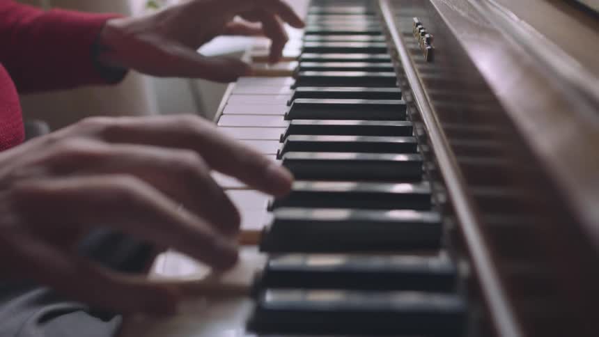 A pianist wearing a red sweater playing a piano keyboard