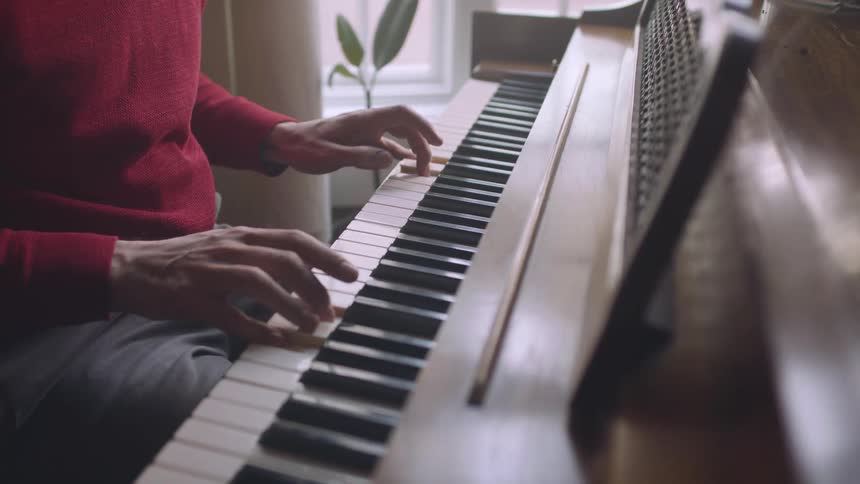 Person in red sweater gently tapping keys playing the piano