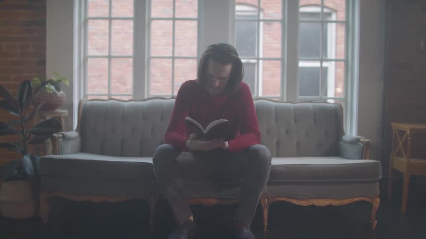 Man sitting on a couch in an apartment reading a book
