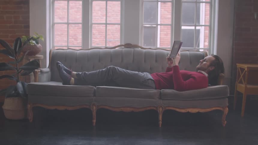A man is laying on a couch reading a book
