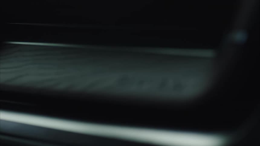The hands of a person on a steering wheel are reflected on the cars dashboard surface