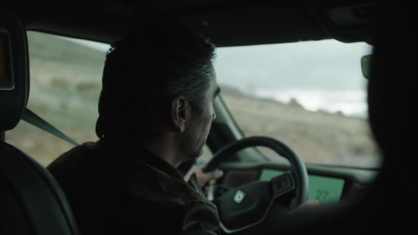 A man driving a vehicle on a rural landscape under an overcast sky