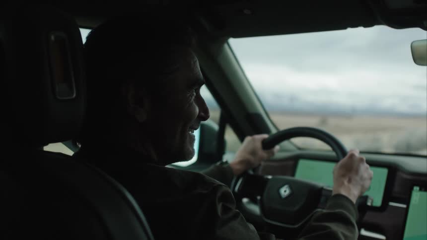 A person is driving a car with both hands on the steering wheel as the dashboard displays two screens with greenlit interfaces