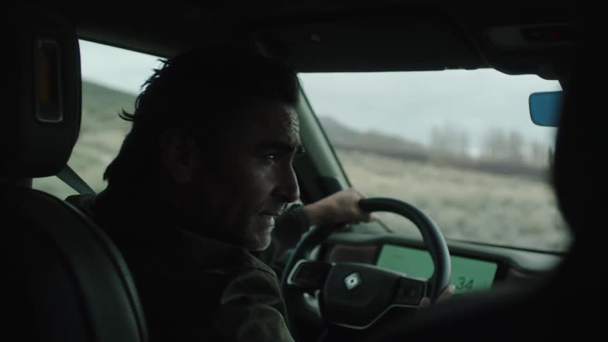 A person drives a vehicle along a road with mountains visible through the windshield