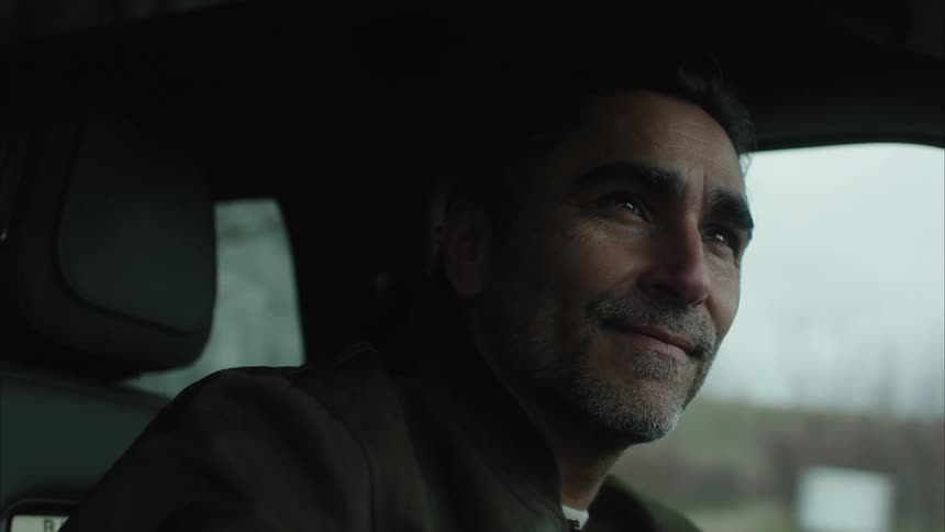 The man is driving down the road and looking out the window