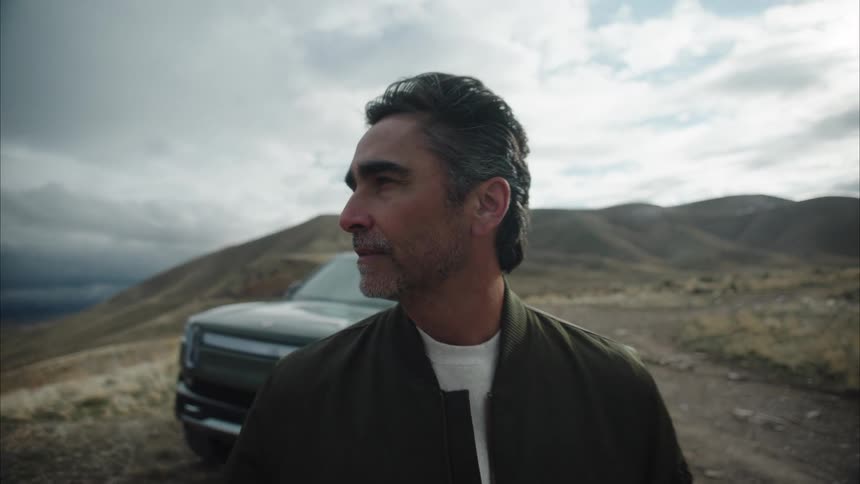 The face of a man standing in a natural environment with a black car parked behind him