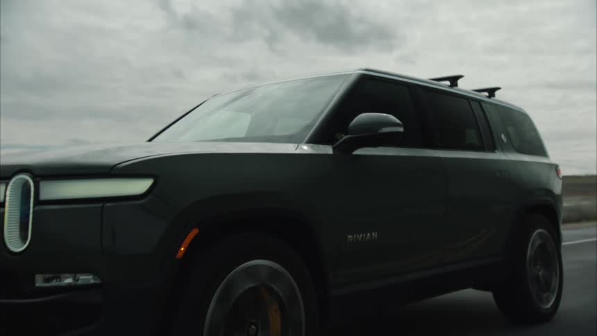 A rivian suv drives along a road with a scenic background showcasing its design and size