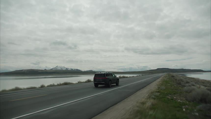 An suv driving on a highway separating two tide pools near a coastal mountain range covered by snow
