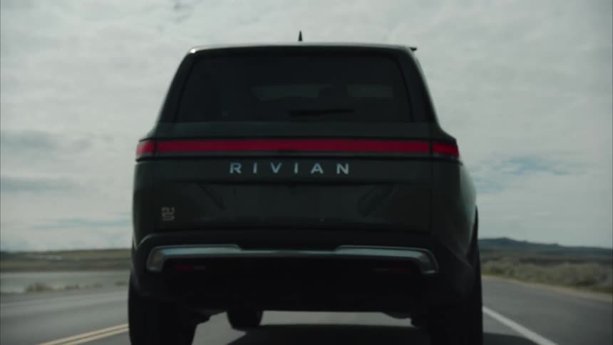 Electric sports utility vehicle travels along a highway passing between two water sources on an overcast day