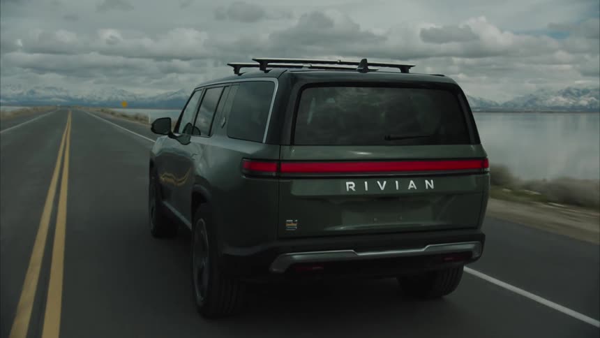 Electric vehicle manufactured by rivian travels along a highway bordered by water on a cloudy winter day