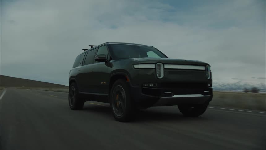 Sports utility vehicle travels along a highway passing a lake and mountains on an overcast day