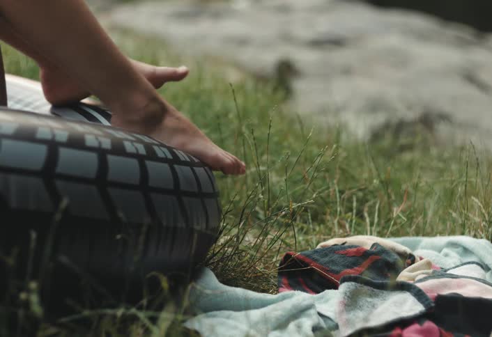 A persons leg rests on a black inflatable ring by a grassy shore with a duck in the background