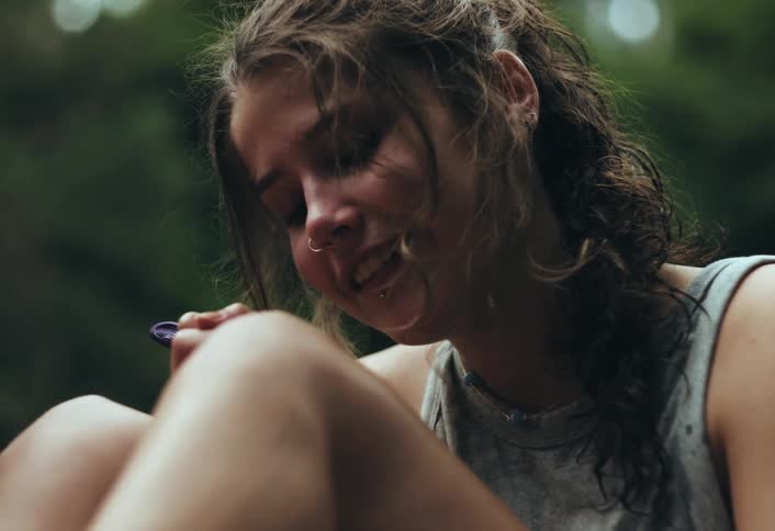 A closeup of teenage friends sitting outdoors talking while one draws with a pen on their knee