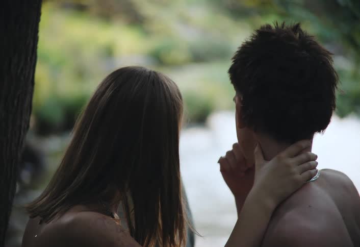 A girl is rubbing a mans head by the stream