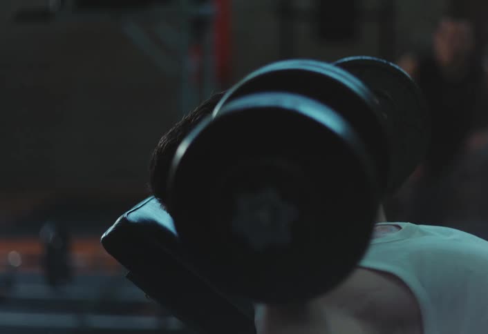 A young man is lying down while lifting weights in a gym