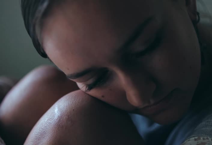 The woman is sitting with her face resting on her knees