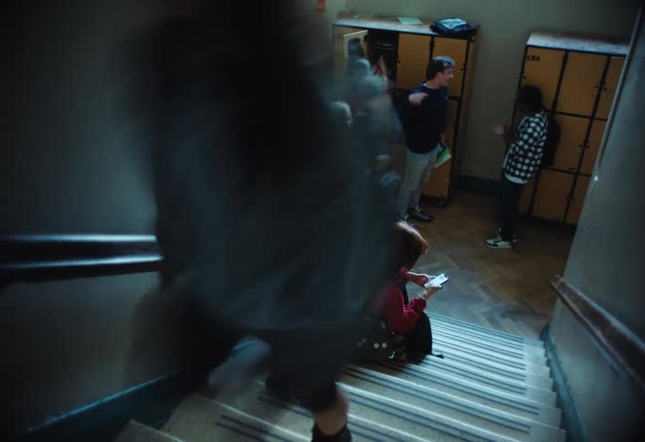 Students walks up and down the stairs near the lockers passing a girl texting on her smartphone