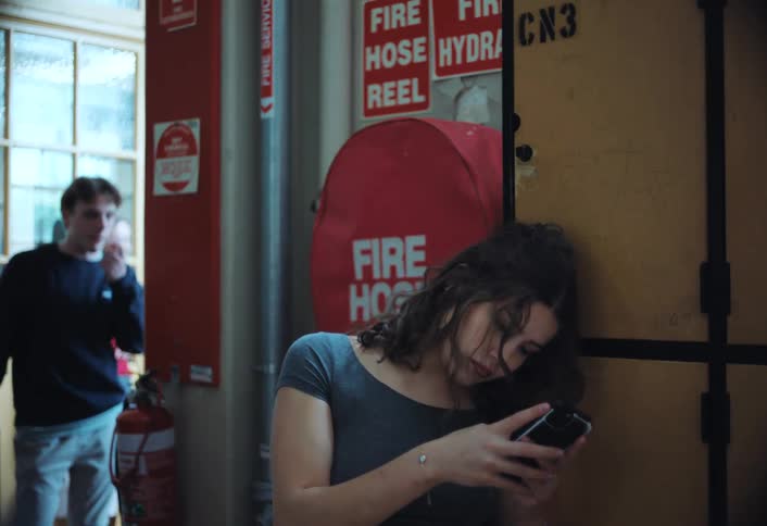 Girl looking at cell phone frowning behind other boys talking