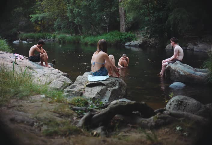 Young man splashes water at an animal while he and his friends enjoy the river near the woods