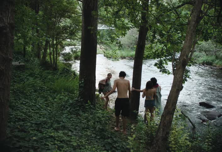 Four individuals walk along a forest trail towards a river ready to take a bath
