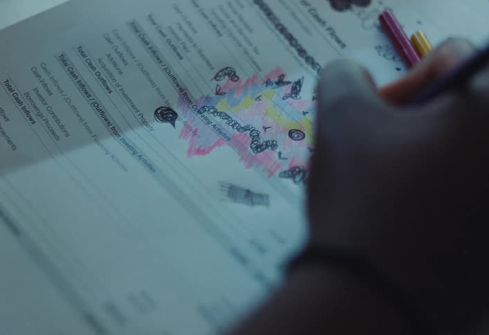 A child is making a drawing on a paper bill using colored pencils