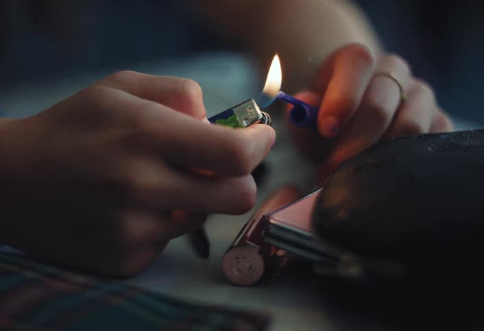 Young person uses the flame from a lighter to melt a pen cap