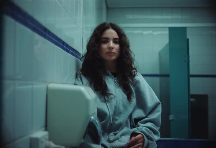Woman stares while leaning against the wall near the hand dryer in a restroom