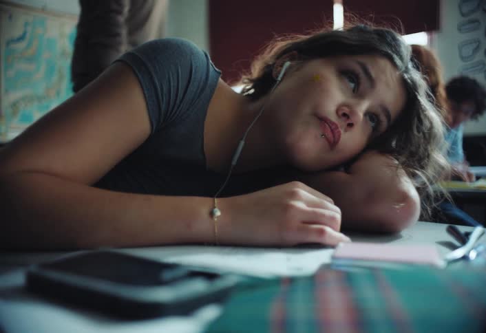 Girl at school lying on the desk with headphones tired and biting her nails